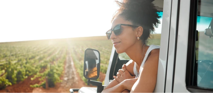 A woman leaning out the window of a truck with a cultivated field in the background.